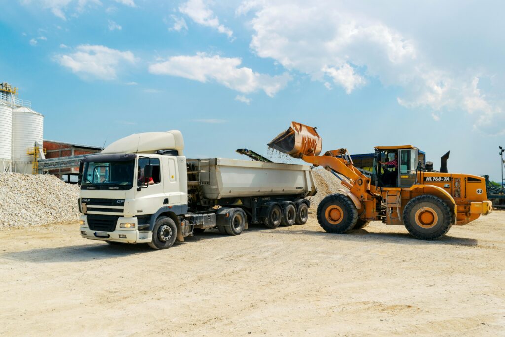 pexels-photo-3089685-3089685 Excavator loading materials into a heavy-duty truck at a sunny construction site.